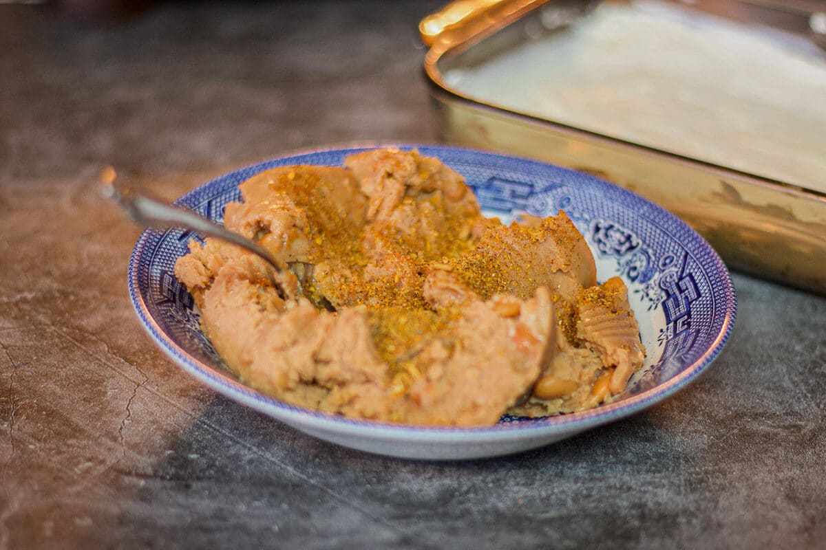 refried beans in a blue bowl with a baking dish full of seasoned cream cheese dip