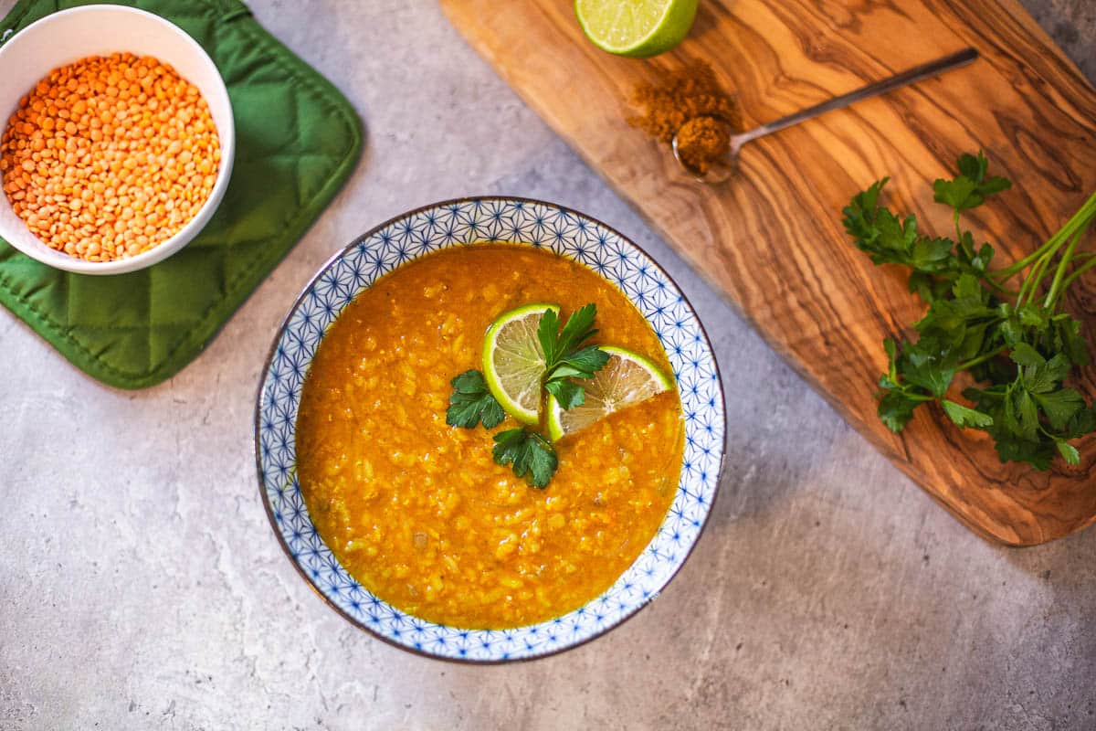 red lentil soup in bowl with lime slices and cilantro beside cutting board full of vcilantro and lime, and small bowl of lentils