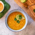 red lentil soup in bowl with lime slices and cilantro beside cutting board and small bowl of lentils