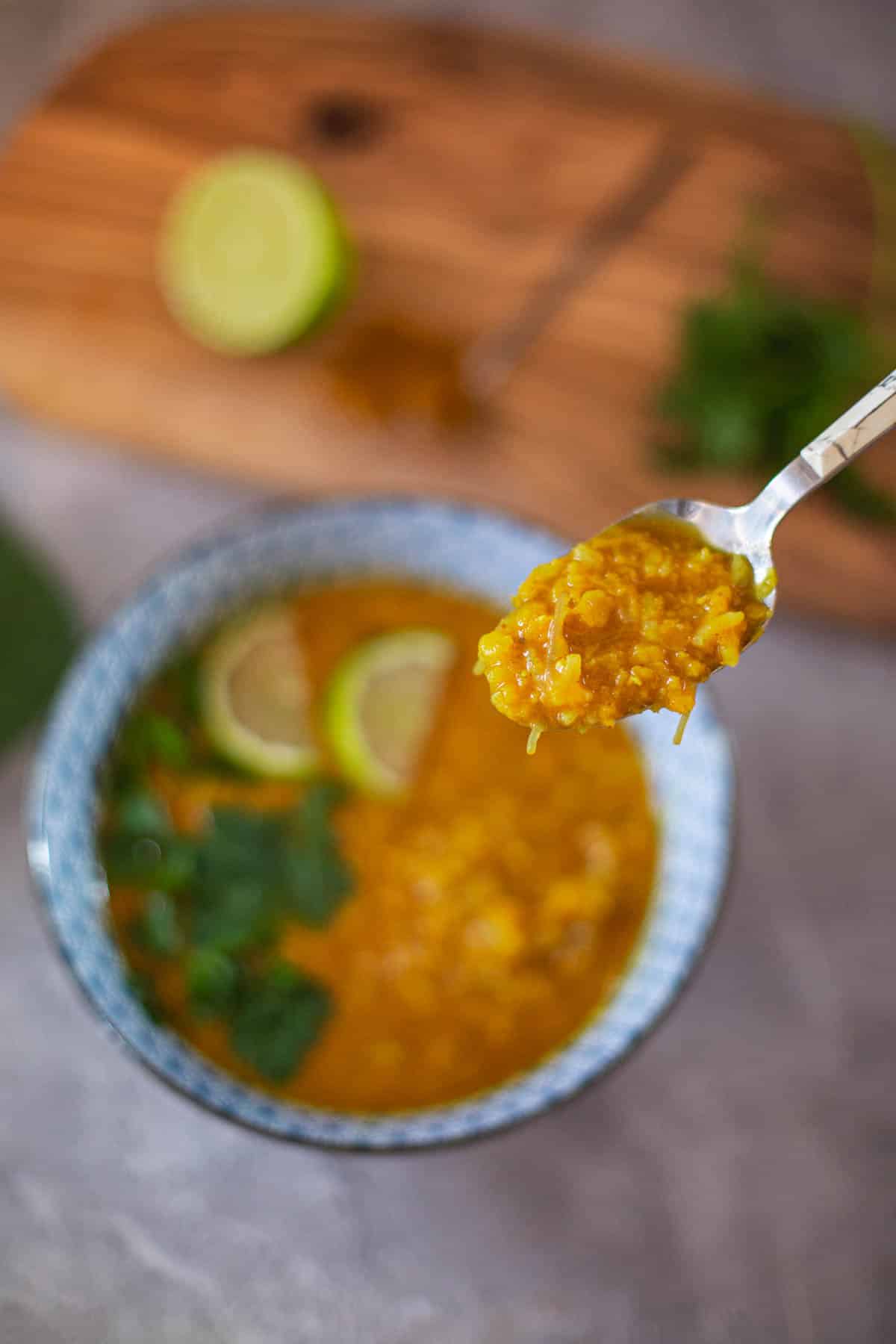 closeup of middle eastern lentil soup in spoon with bowl and cutting board in background