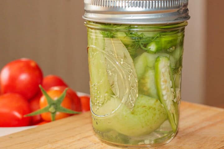 pickled green tomatoes in a jar with red tomatoes in the background