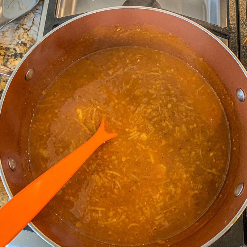 lentil soup in a brown pot with an orange spoon