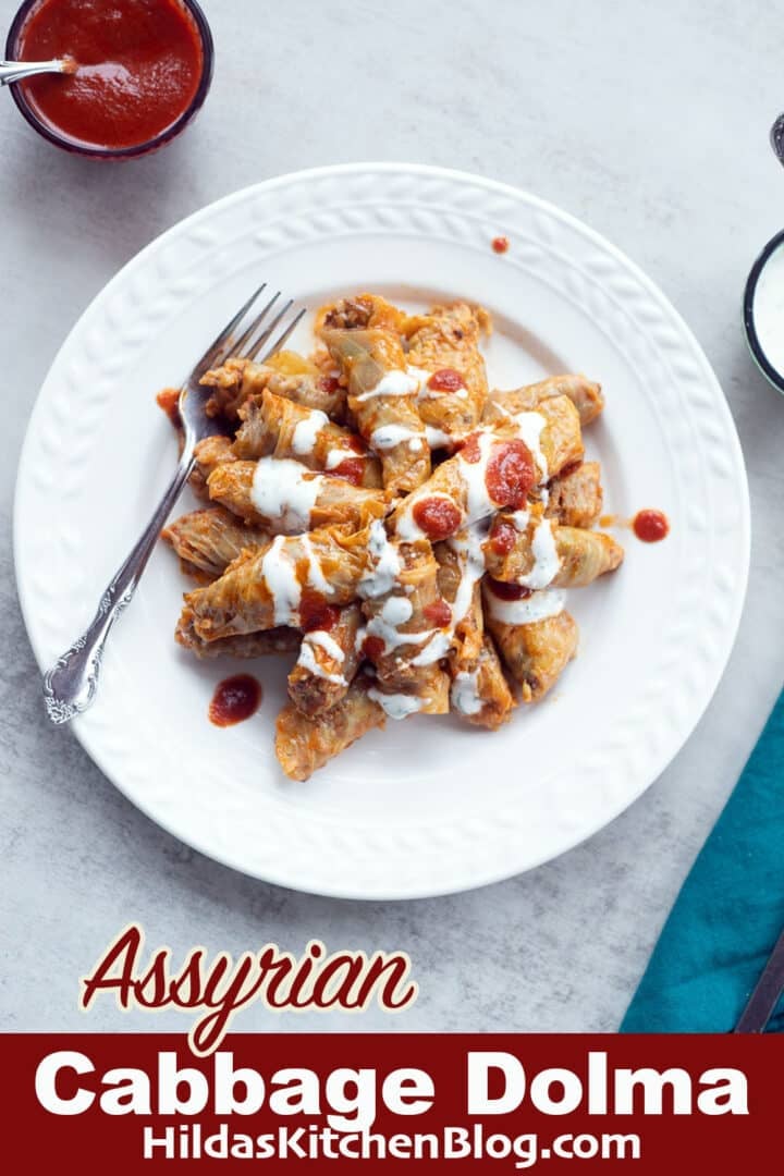 Assyrian cabbage dolma on a white plate with red and white sauce on the side.