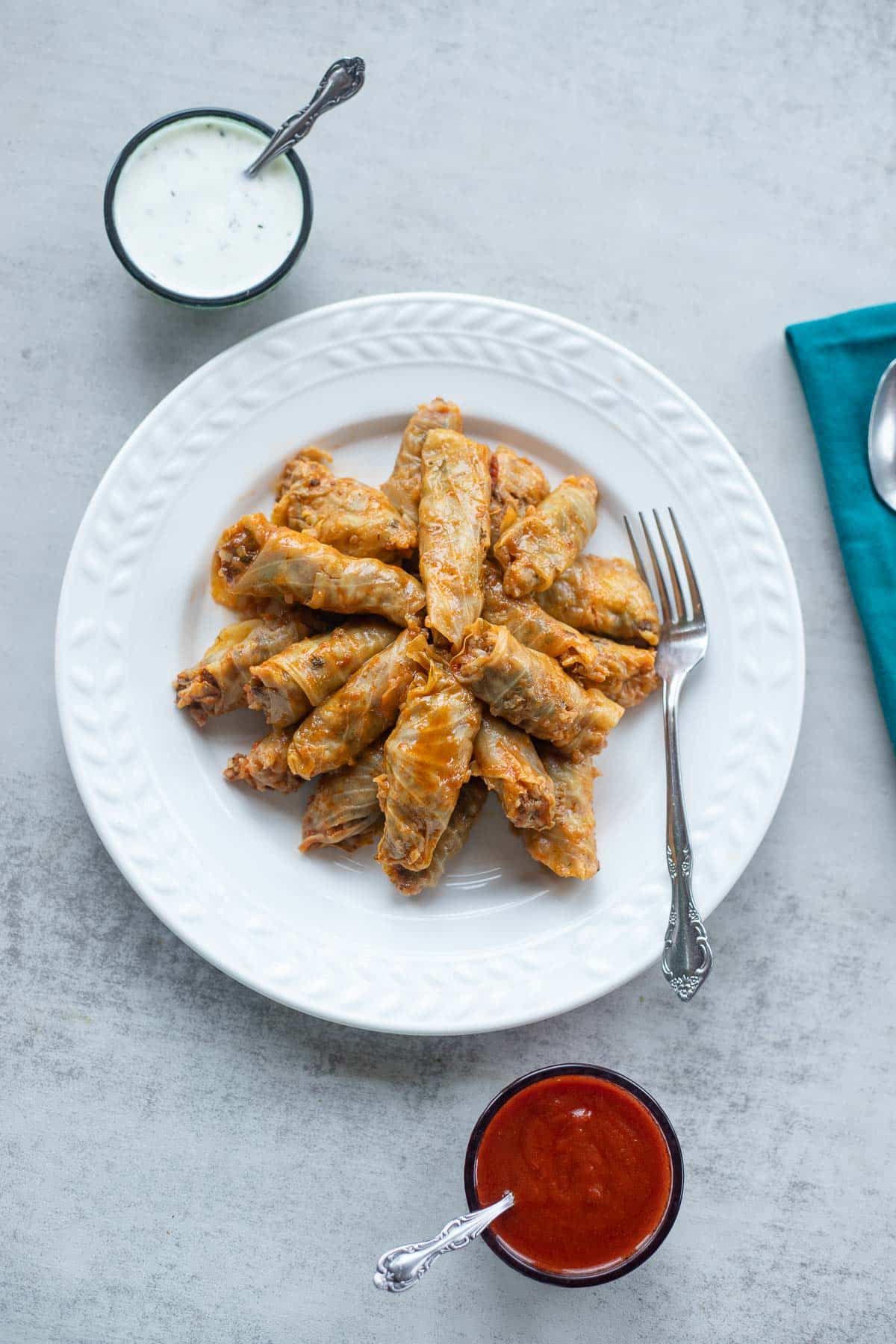 cabbage dolma on a white plate with red sauce and yogurt sauce on the side.