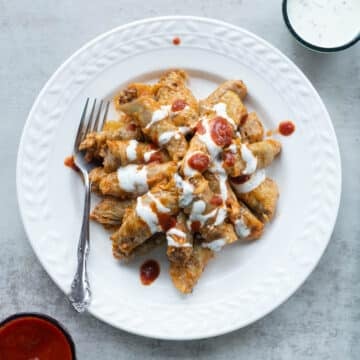 Assyrian cabbage dolma on a white plate with red and white sauce on the side.