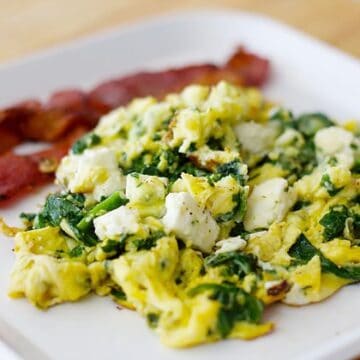 spinach and eggs on a white plate with bacon slices