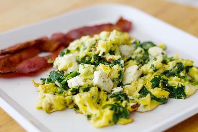 spinach and eggs on a white plate with bacon slices