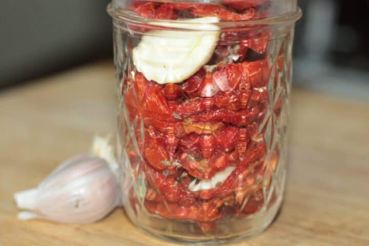 sun-dried tomatoes in a jar topped with a garlic clove