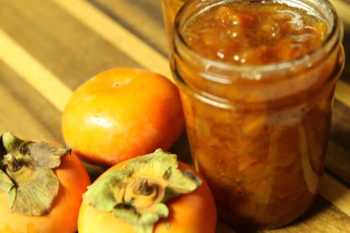 persimmon preserves in an open jar with more fruit on the side