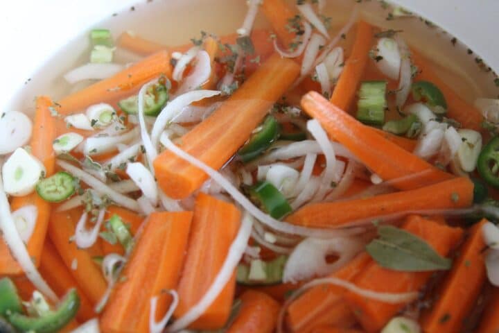 sliced carrots, onions, and herbs in a pot of liquid