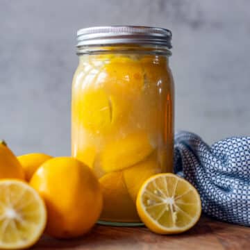 preserved moroccan lemons in a jar with more lemons and a blue towel next to it