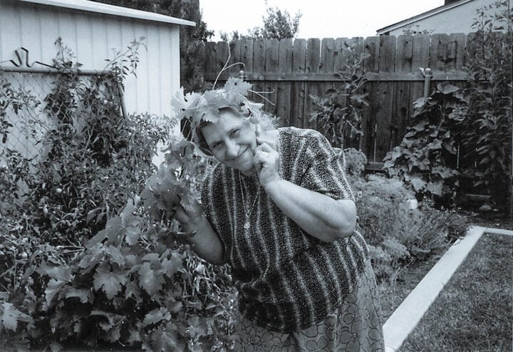 an old lady in the garden with grape leaf vine around her head