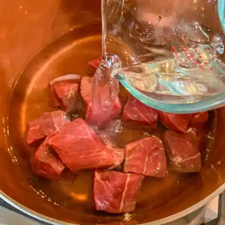 pouring water over cubed meat in a pot