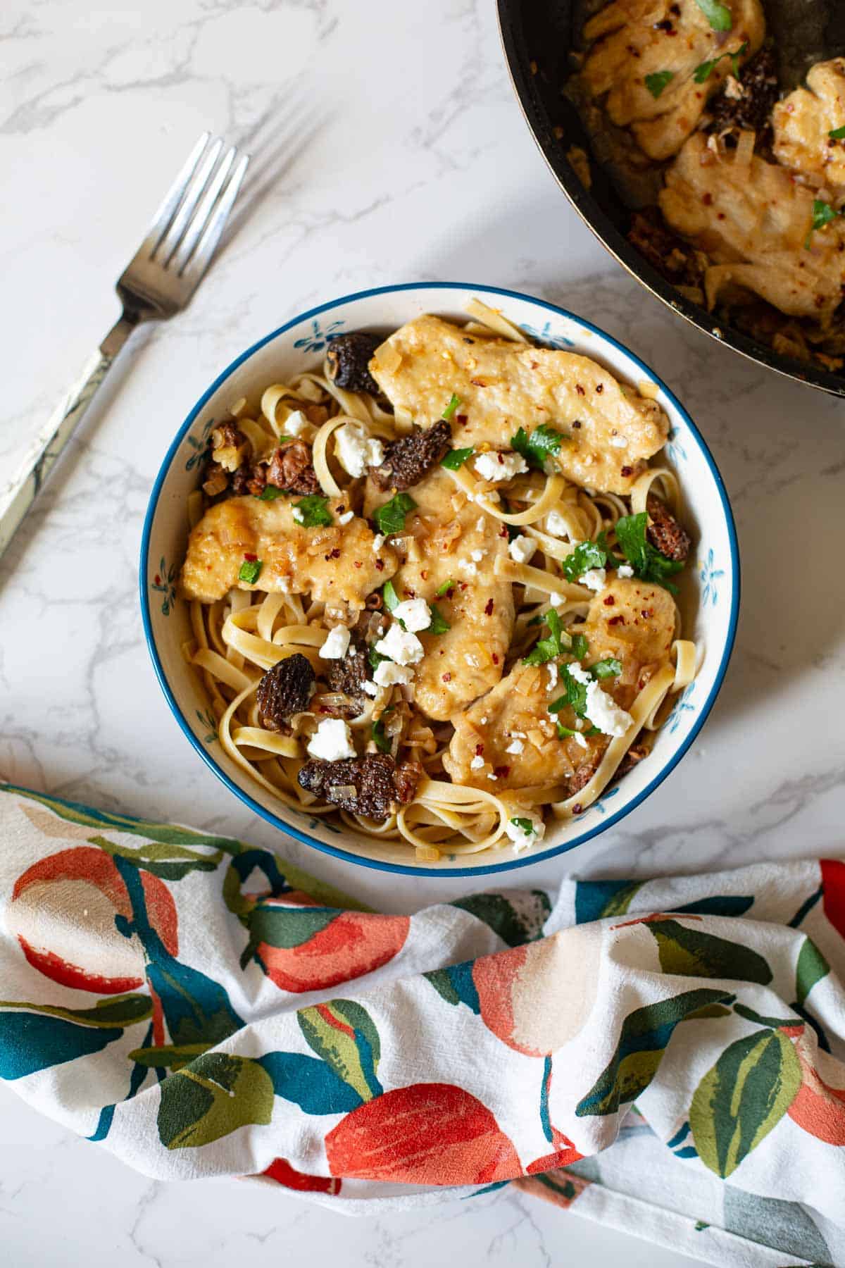 chicken scallopini over pasta with morel mushrooms in a blue rimmed bowl with a fork next to it