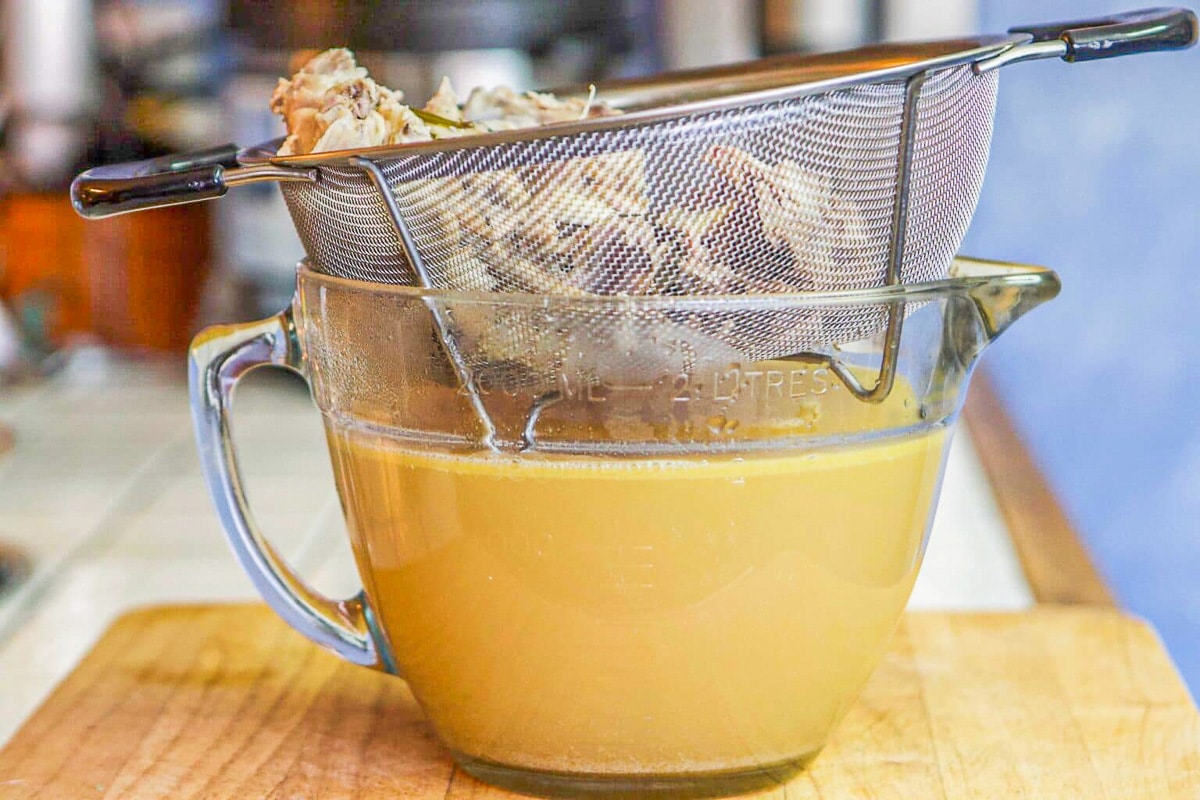 chicken broth in a large measuring cup with strainer over it