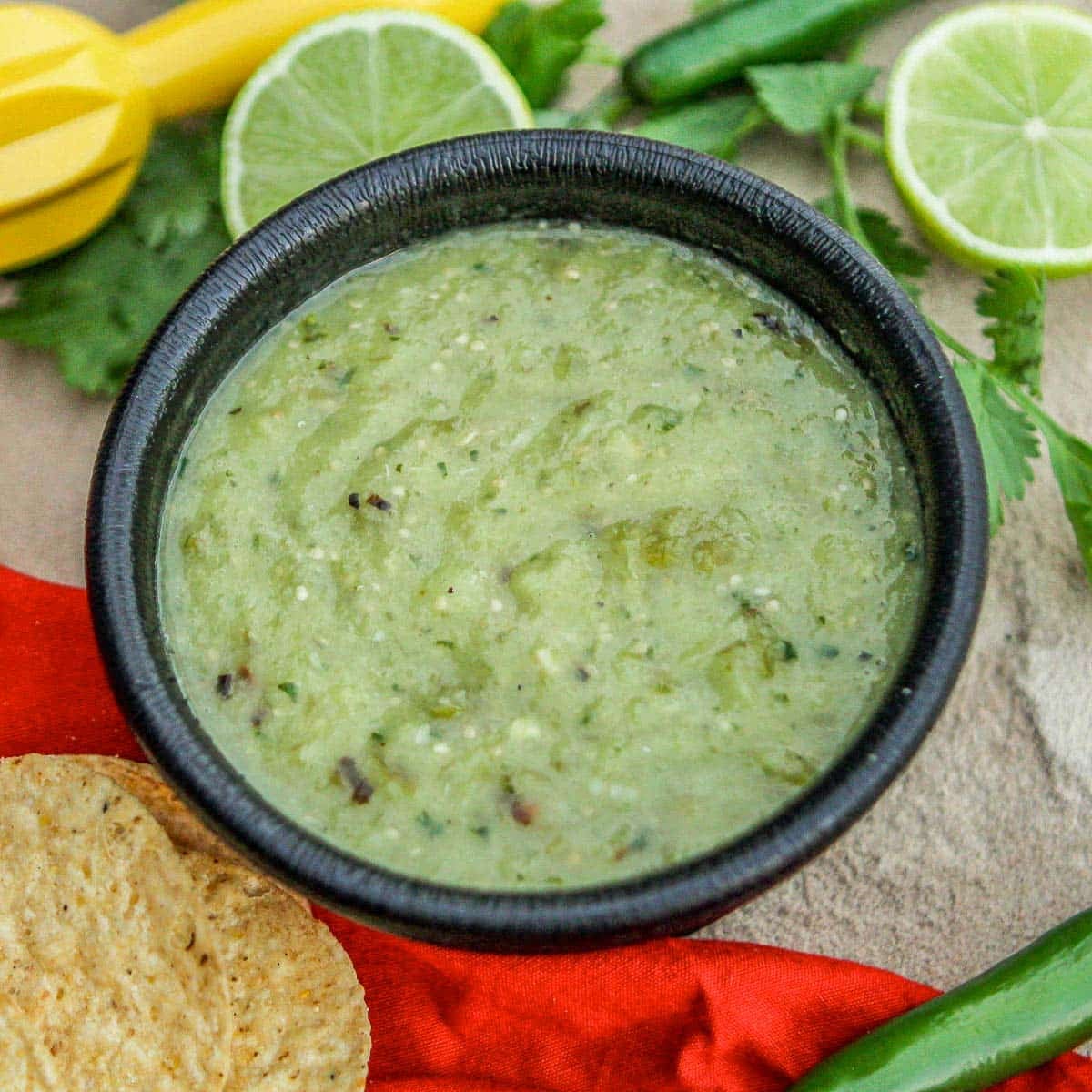 salsa verde with limes and chips around it.