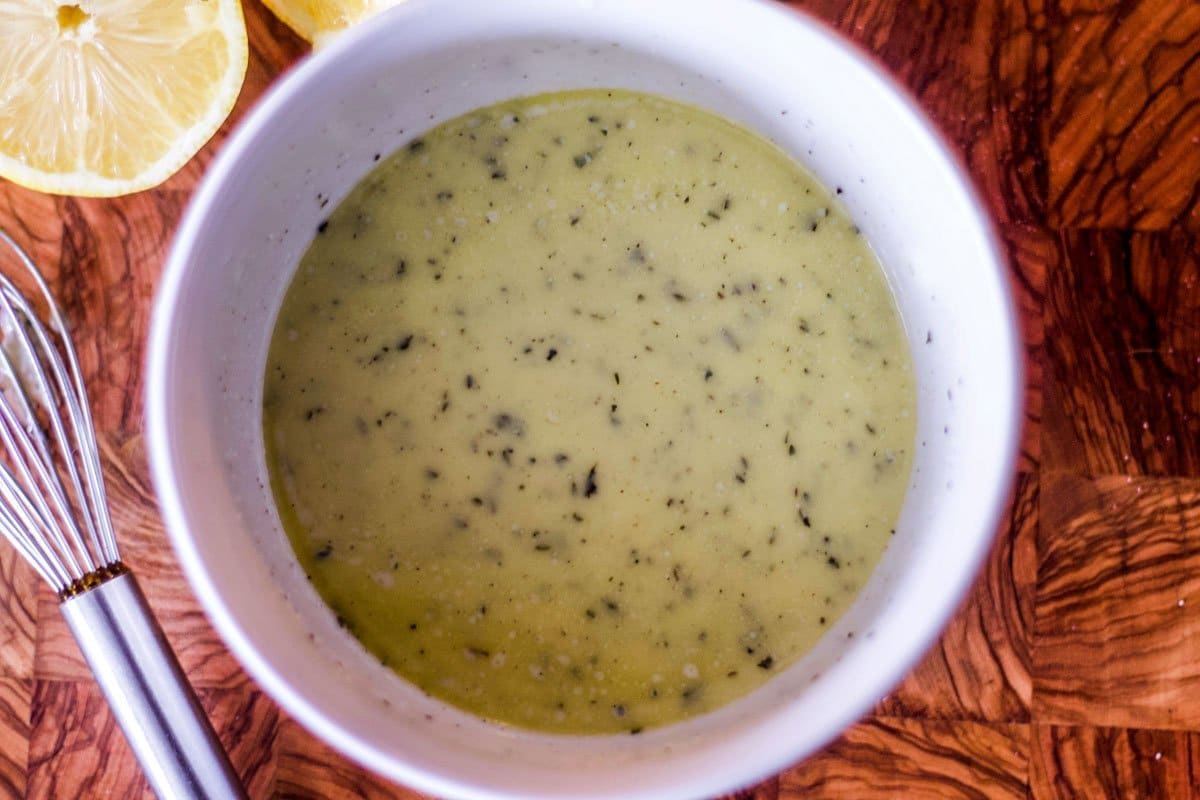 dressing in a white bowl with a whisk and lemon slices on the side