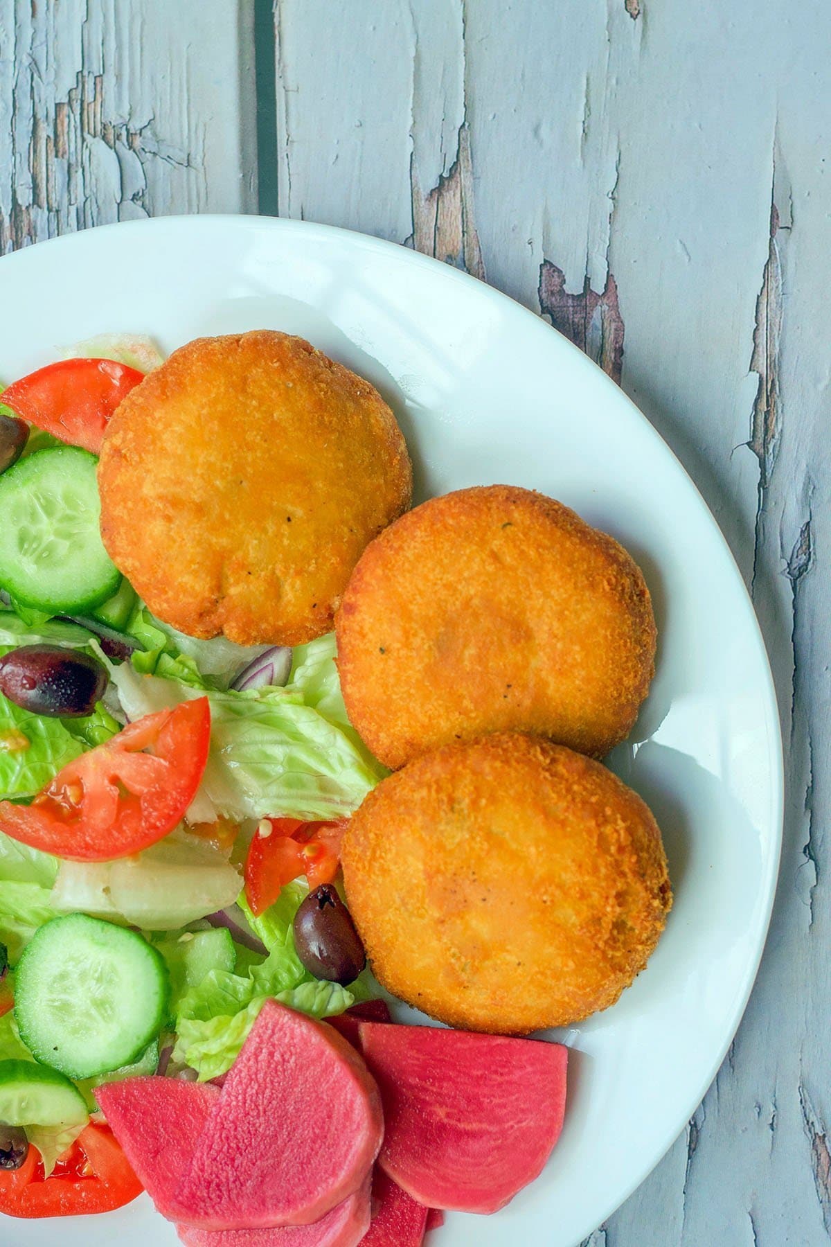 3 potato chops on a white plate with salad