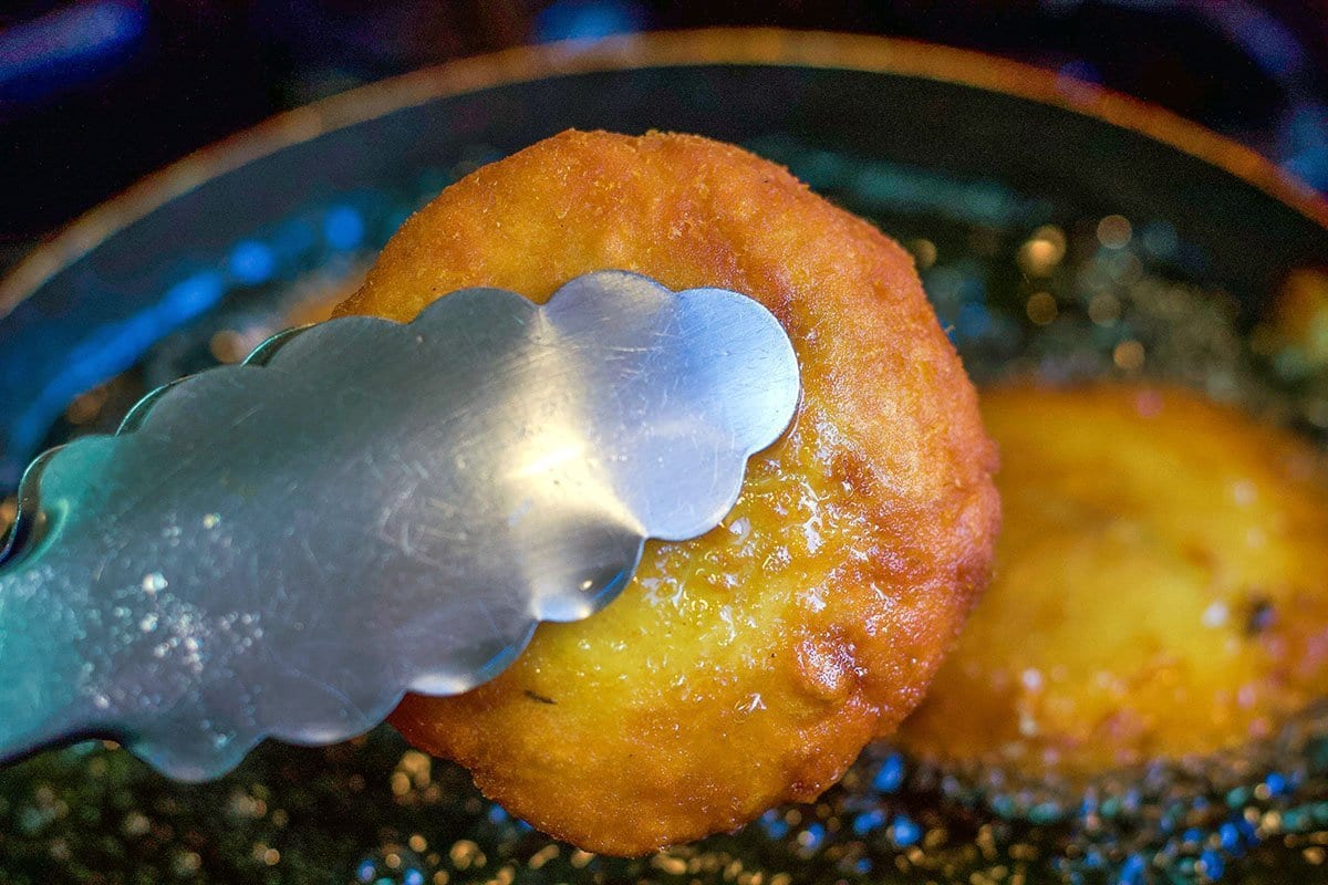 potato chop being removed from hot oil with tongs.