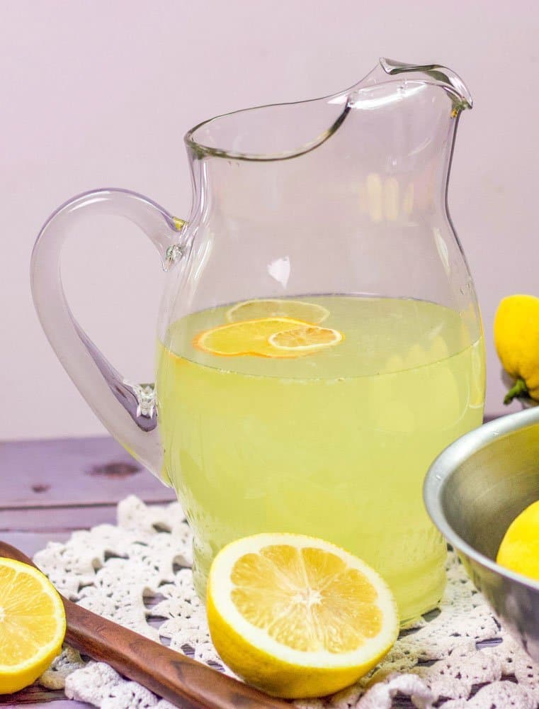 lemonade jug on a doily with sliced lemons around it