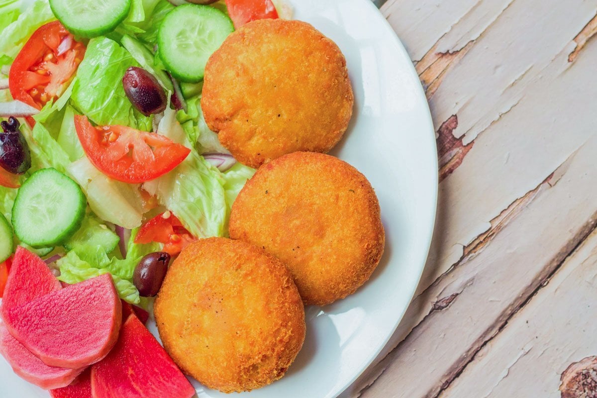 3 potato patties on a white plate with a salad