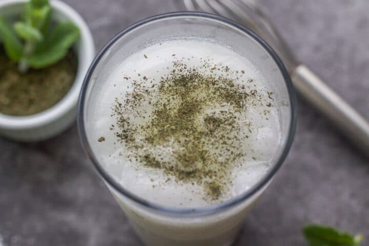 yogurt drink called ayran in a glass on the counter with mint and whisk