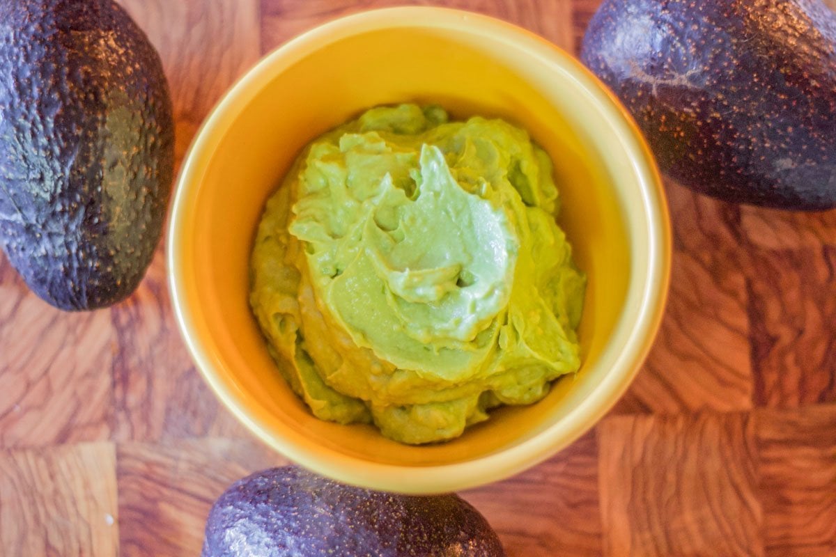 creamy guacamole in a yellow bowl with 3 avocados