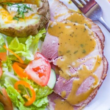 honey mustard sauce over ham on a plate with salad and baked potato