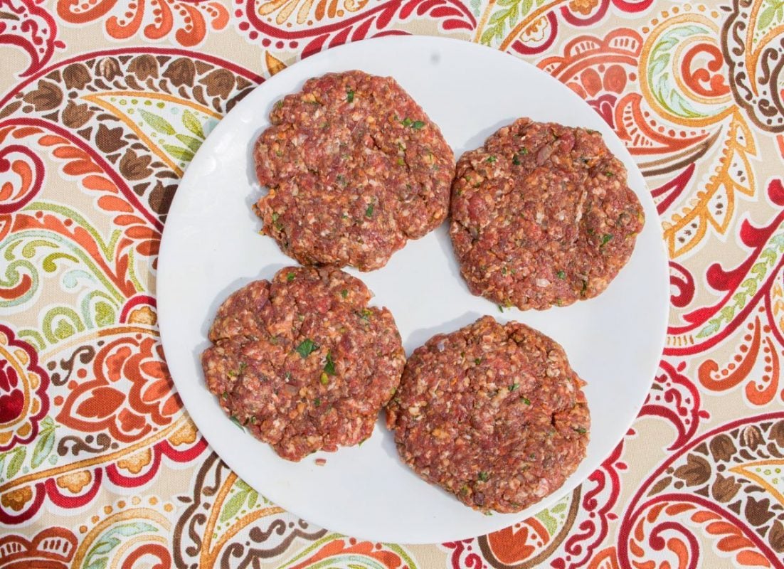 four raw meat patties on a white plate