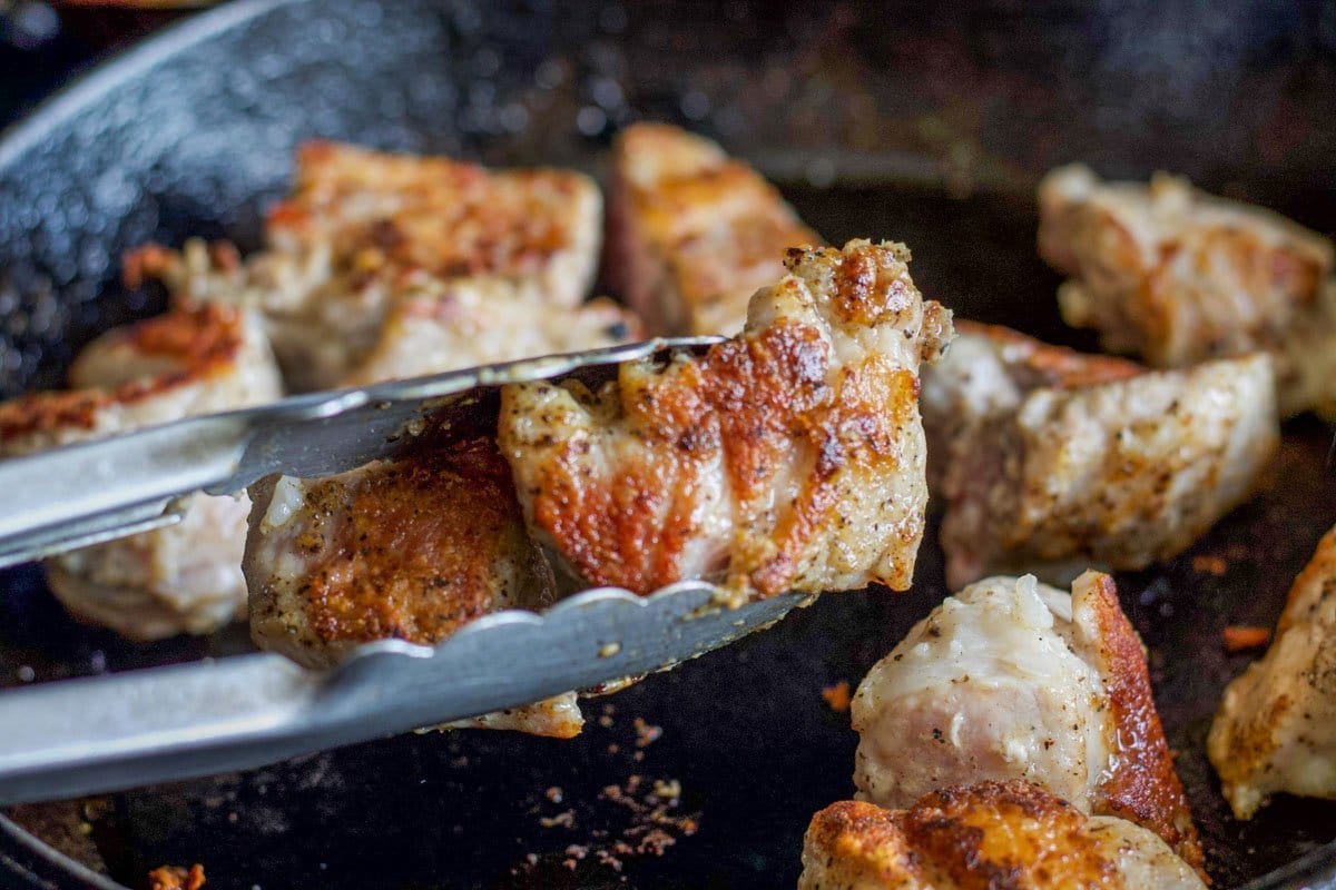 seared pork chunks being held with tongs