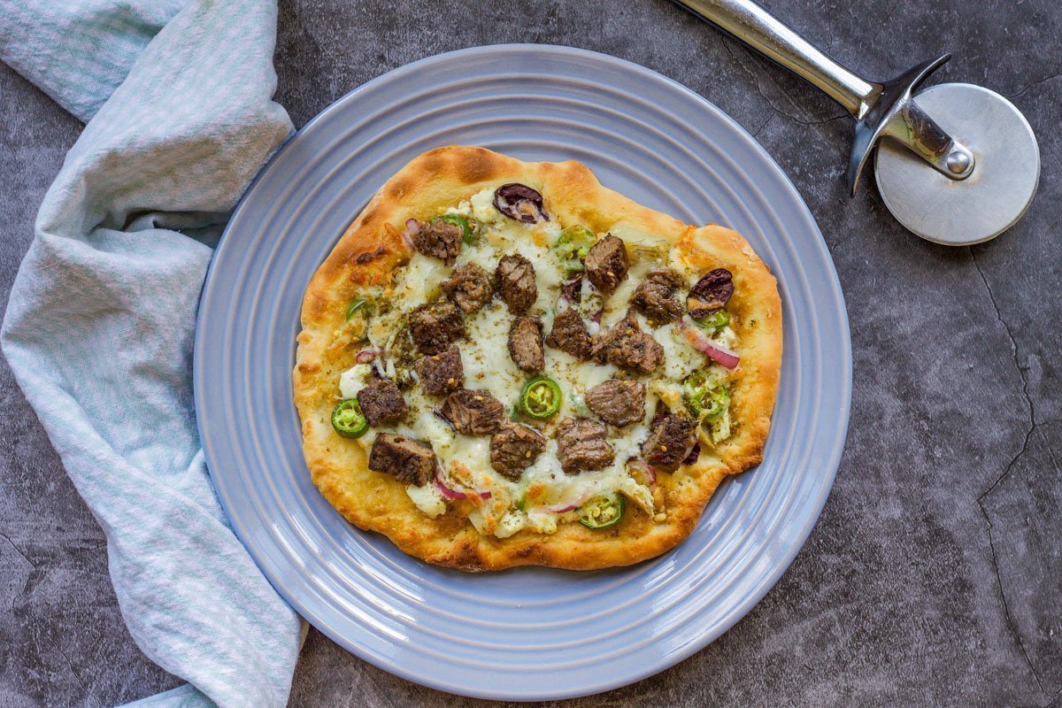 pizza on a blue plate with a dishtowel and pizza wheel on the side