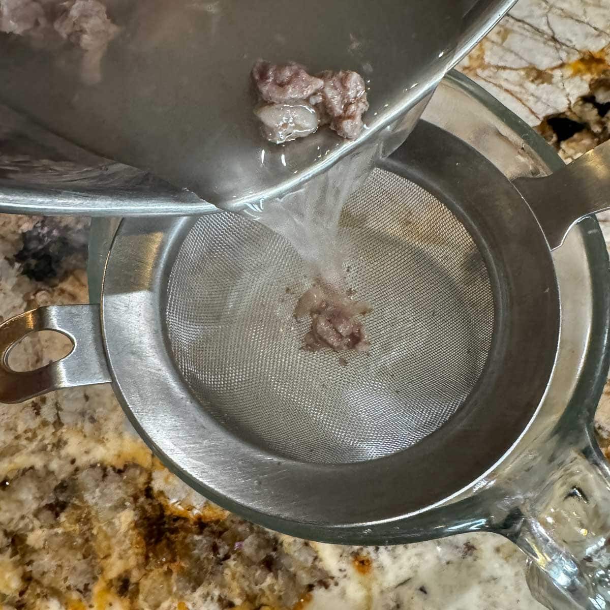 broth being strained from a pot with diced meat.