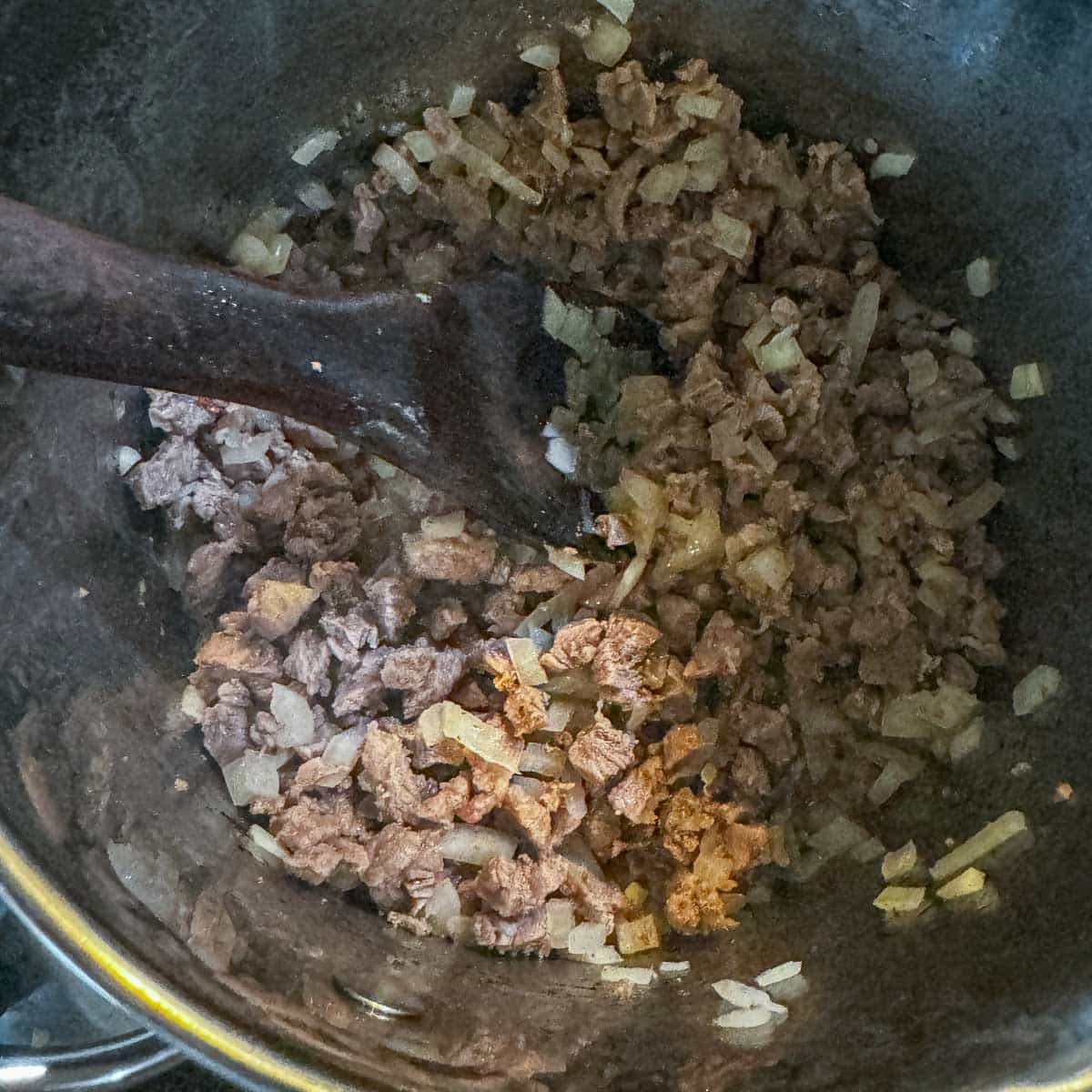 sauteeing diced meat and onion in a pot.