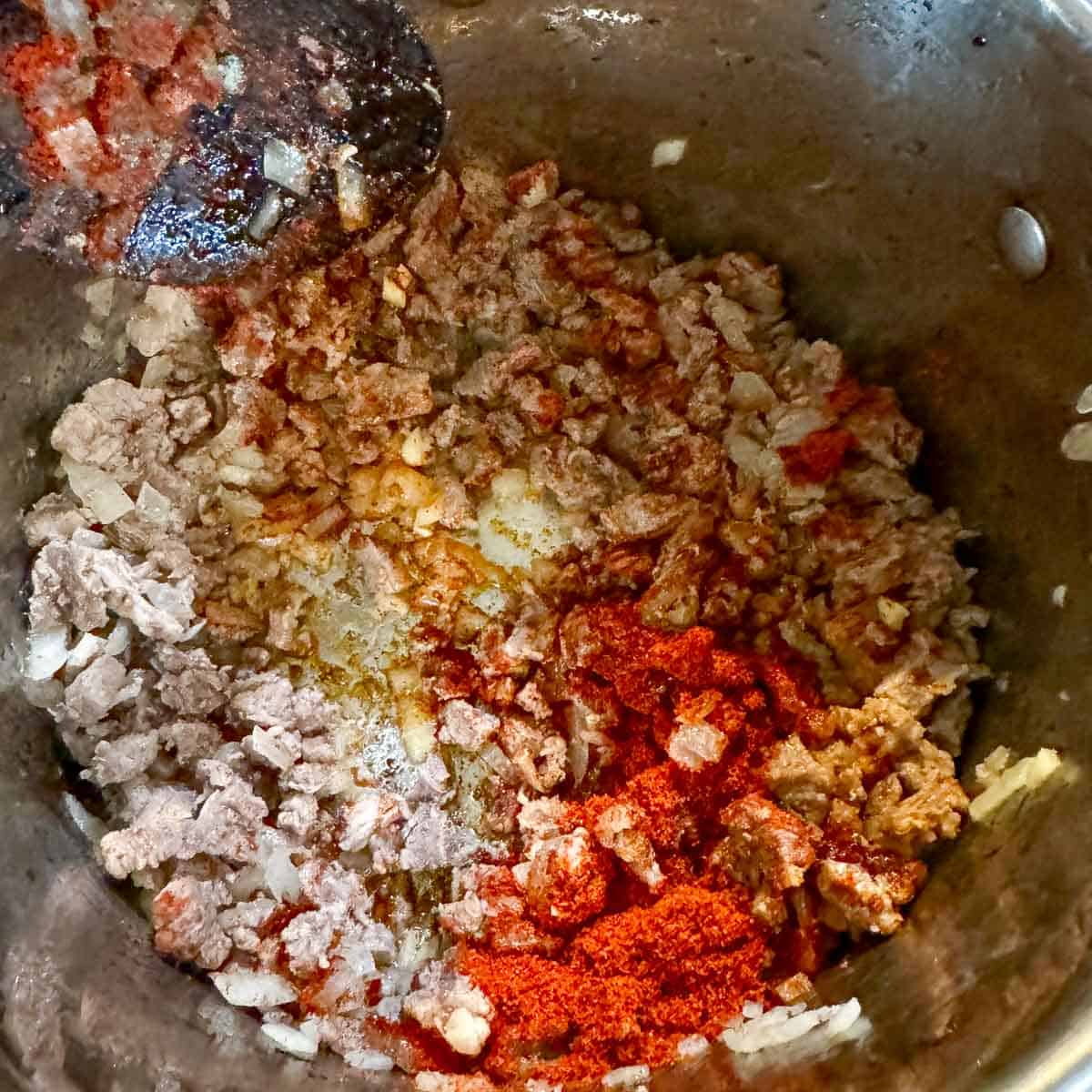 diced meat and onions being stirred with spices in a pot.