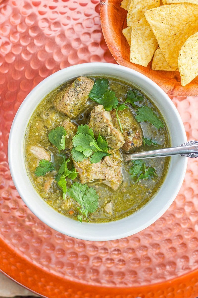 a bowl of chili verde in a white bowl and chips