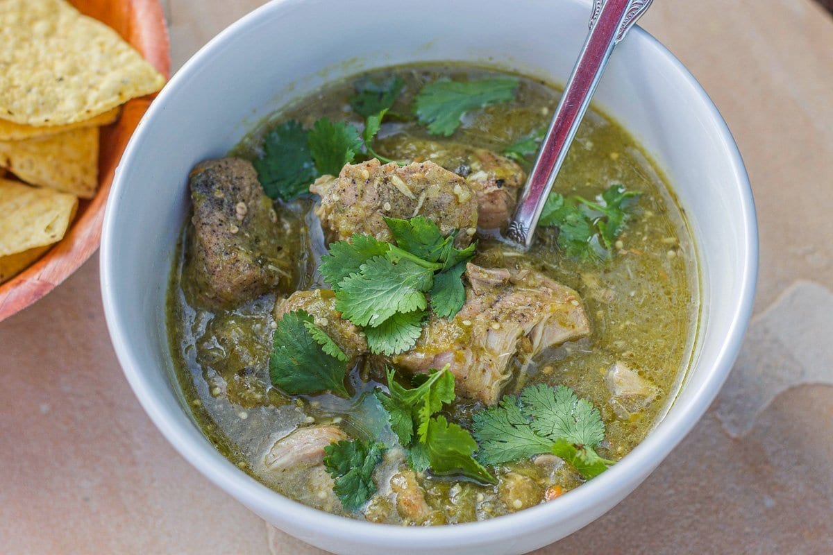 chili verde in a white bowl with chips on the side