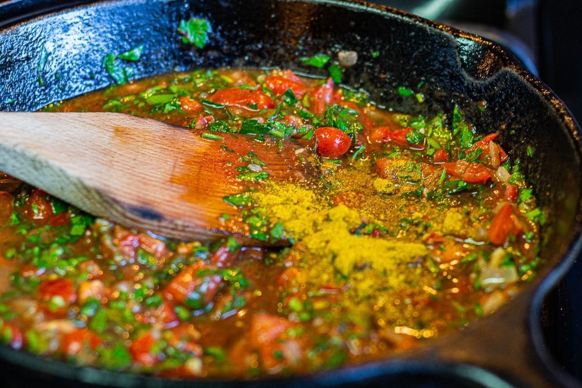sauce being stirred in a cast-iron pan