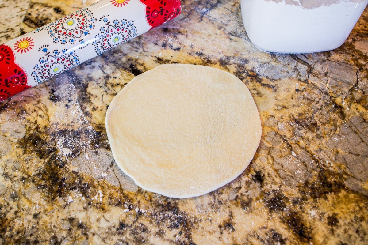 flattened round dough with a colorful rolling pin behind it