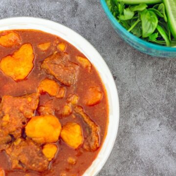 curry in a white bowl with herbs on the side