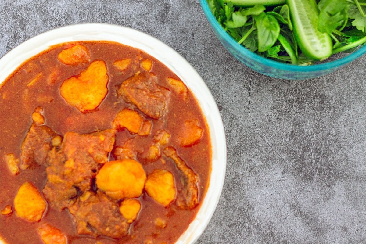 curry in a white bowl with herbs on the side