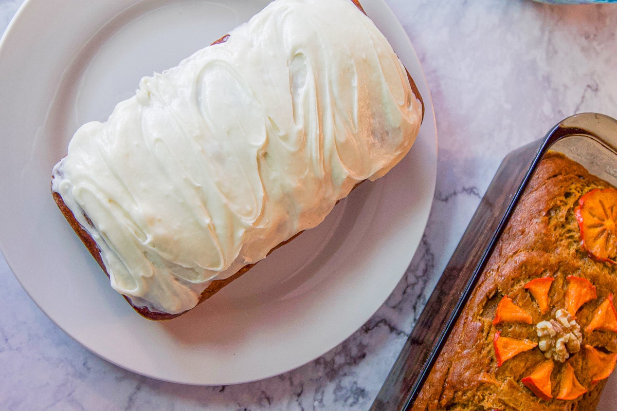 frosted persimmon bread on a white plate with an  additional loaf on the side