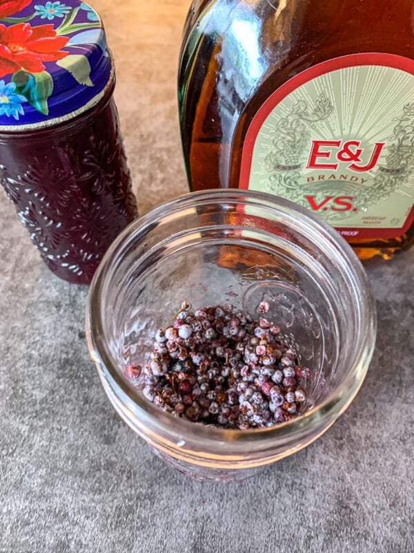 elderberries in a jar with brandy and syrup in the background