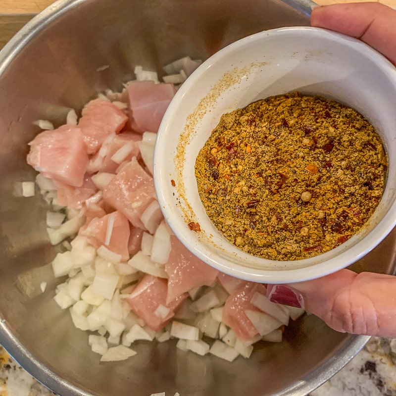 pouring spices over chicken in a pot