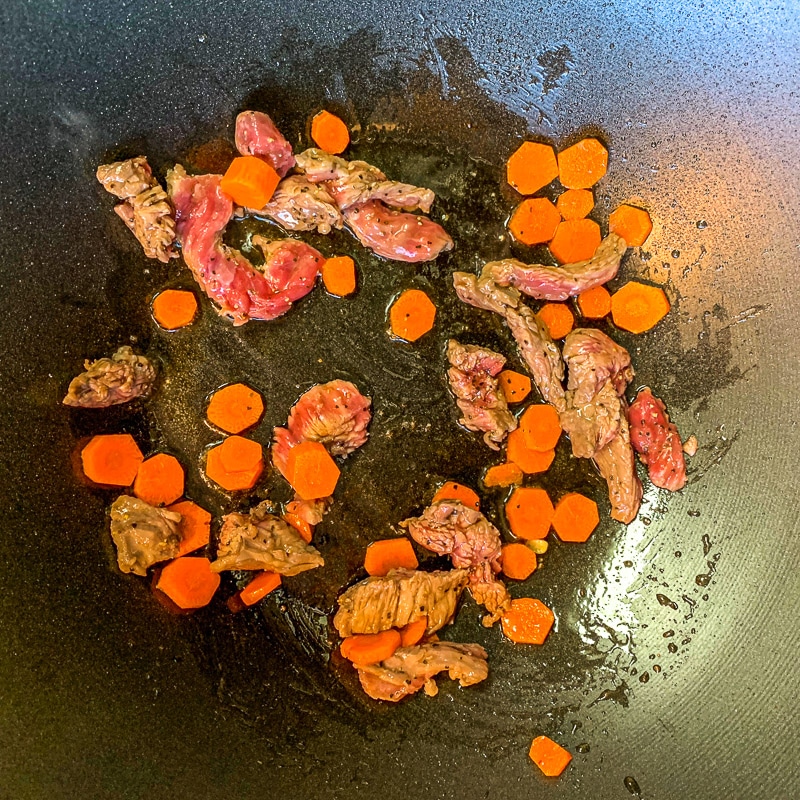 meat and carrots being cooked in a pan