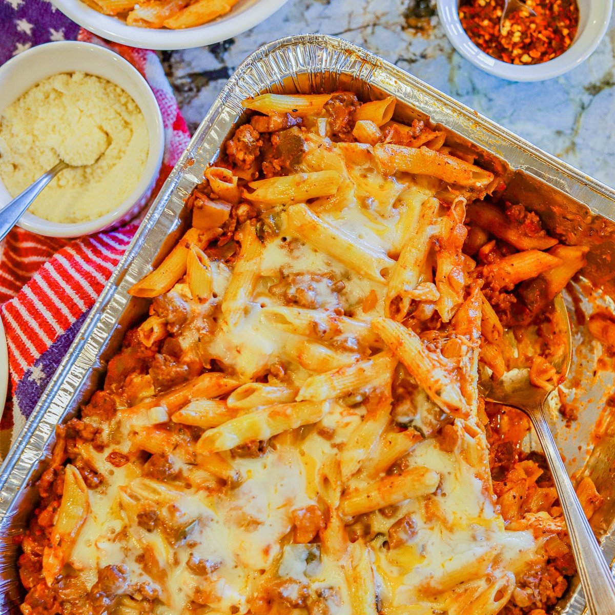 A closeup of a pan of baked penne pasta covered in cheese and a red tomato sauce