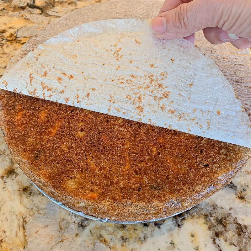 peeling parchment paper from frosted carrot cake with pineapple