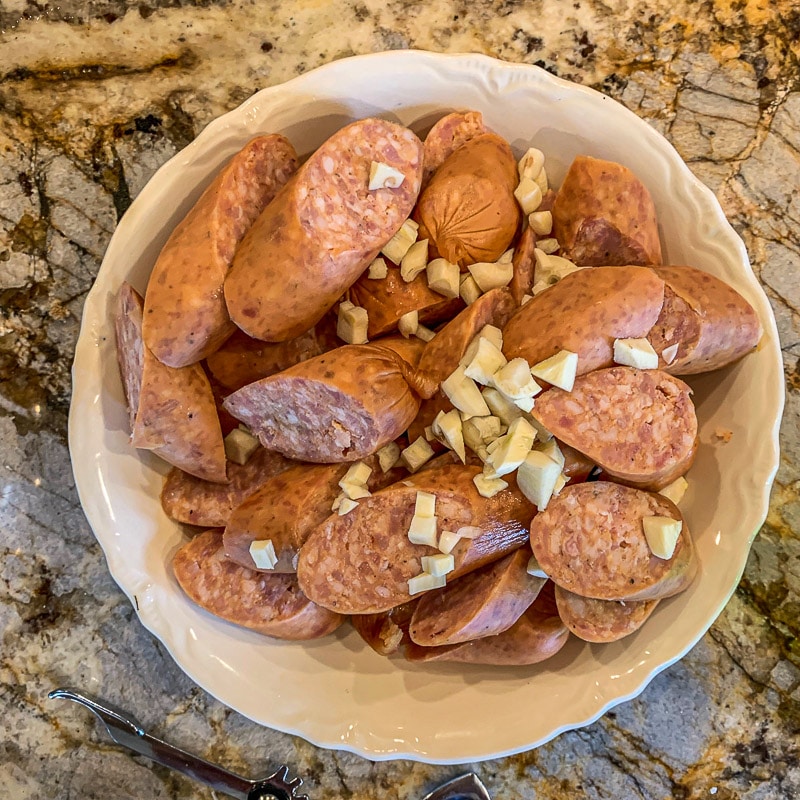 chopped kielbasa topped with garlic cloves in a white plate