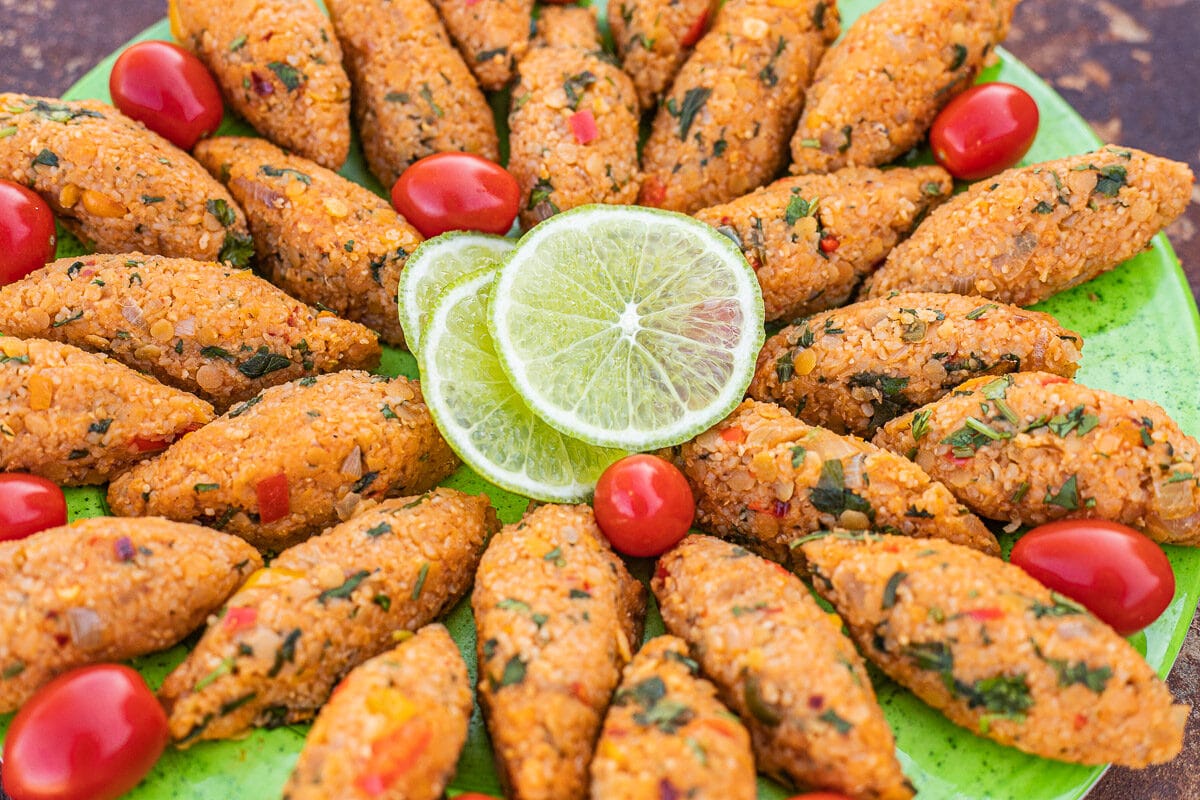 Mercimek Koftesi on a green plate with cherry tomatoes and sliced lime