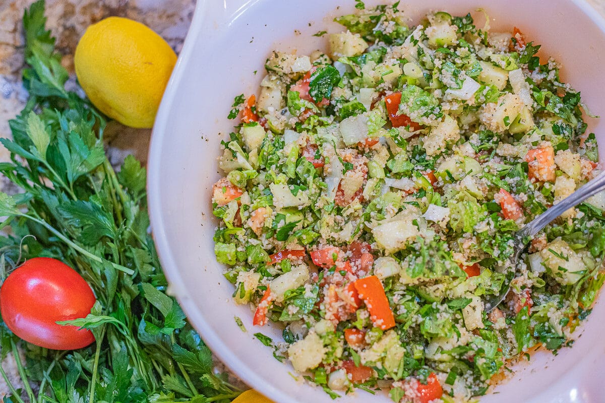 Tabouli salad in a bowl with vegetables around it