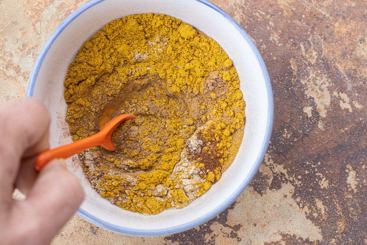 stirring biryani spice in a bowl with an orange spoon